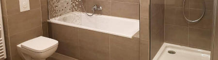Modernes, beige gefliestes Bad mit einer Wandtoilette auf der linken Seite, einer Badewanne mit einer dekorativen Glasscheibe in der Mitte und einer begehbaren Dusche mit einer Glastür auf der rechten Seite.